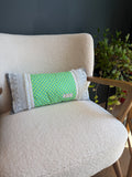 Coussin long fait main Lyli Créarti, tissu imprimé écailles vert et bleu, bandes latérales en dentelle grise, posé sur fauteuil en bouclette blanche