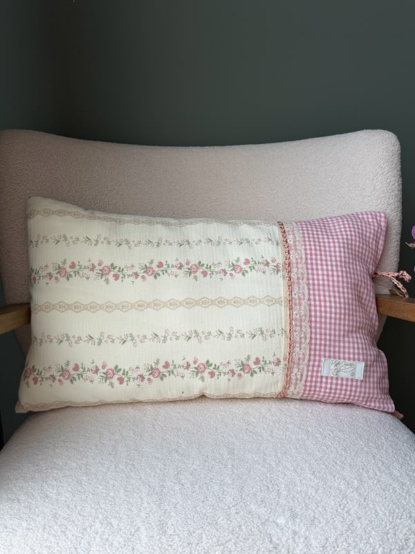 Coussin rectangulaire fait main Lyli Créarti, tissu à motif floral vintage rose sur fond ivoire et vichy rose, galon dentelle, posé sur fauteuil en bouclette blanche