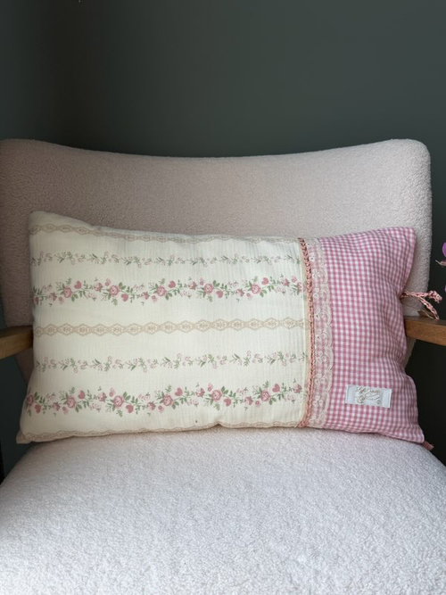 Coussin rectangulaire fait main Lyli Créarti, tissu à motif floral vintage rose sur fond ivoire et vichy rose, galon dentelle, posé sur fauteuil en bouclette blanche