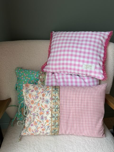 Coussins fait main Lyli Créarti, tissus vichy rose à volant, imprimé fleuri turquoise et vichy ivoire, empilés sur fauteuil en bouclette blanche