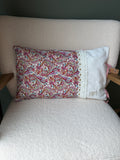 Coussin rectangulaire fait main, tissu imprimé cachemire rose et rouge et lin blanc rayé, dentelle fleurie et étiquette artisanale, posé sur fauteuil en bouclette blanche