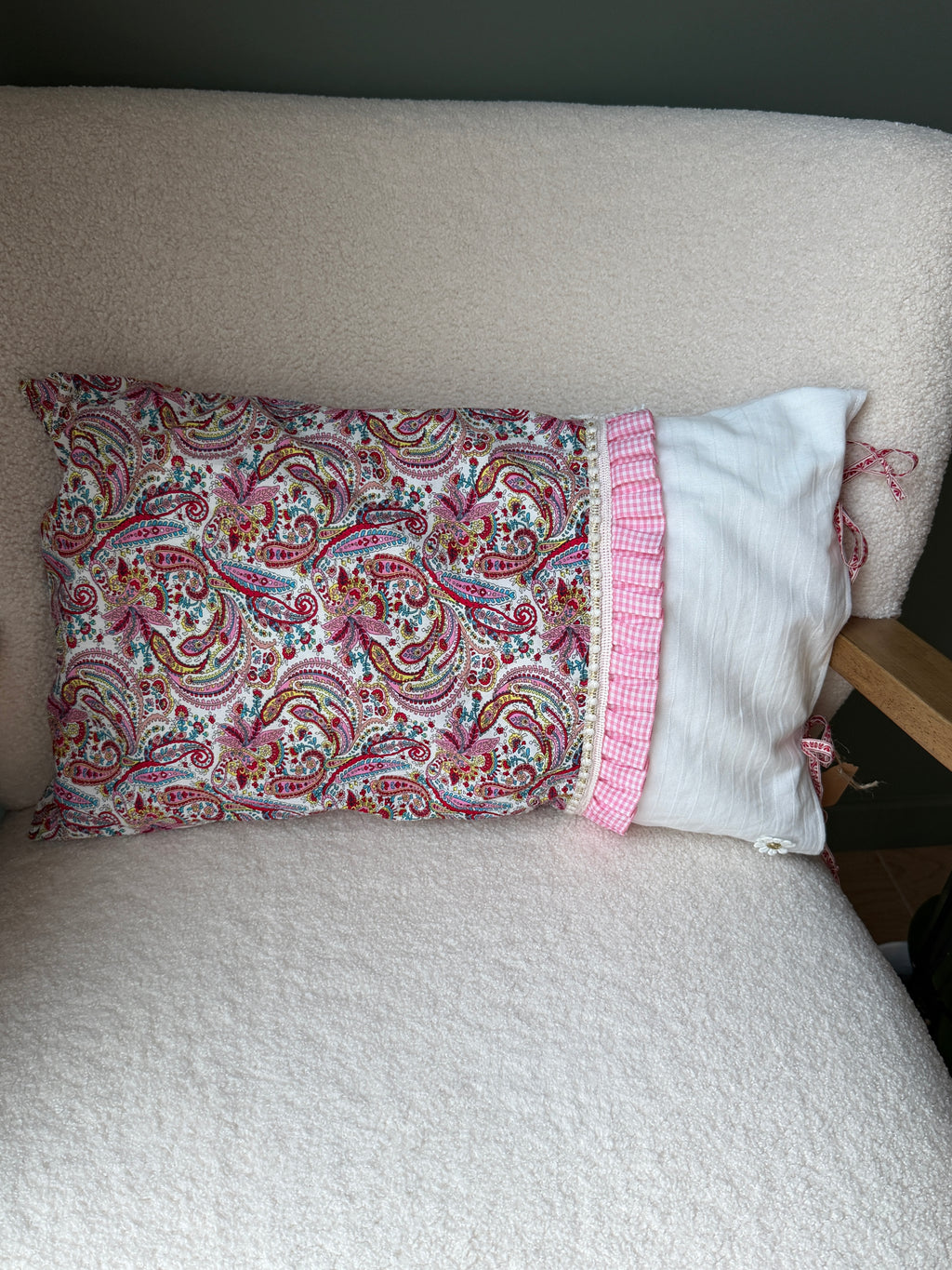 Coussin rectangulaire fait main, tissu imprimé cachemire rose et lin blanc, volant à carreaux vichy rose et rubans, posé sur fauteuil en bouclette blanche