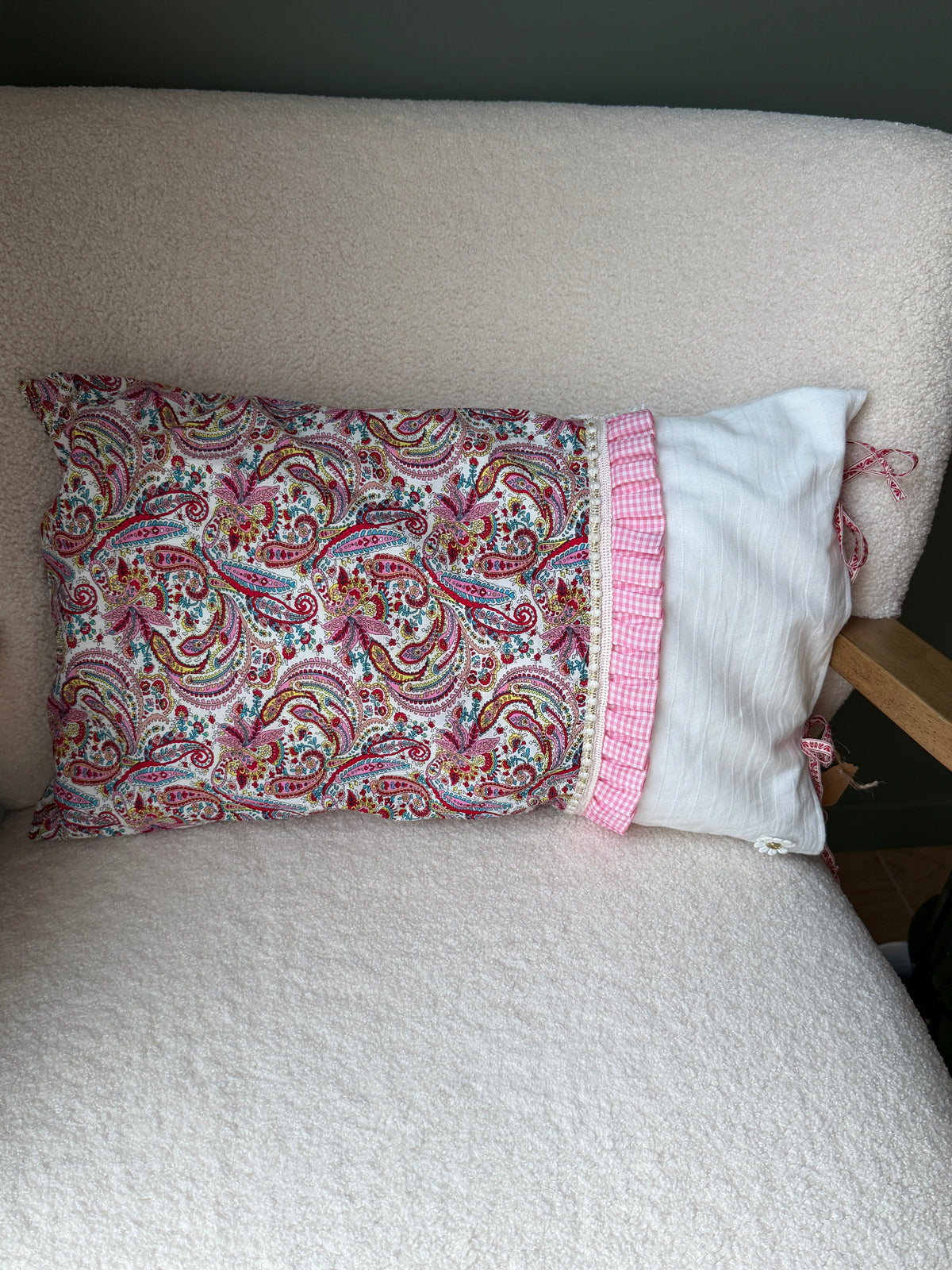 Coussin rectangulaire fait main, tissu imprimé cachemire rose et lin blanc, volant à carreaux vichy rose et rubans, posé sur fauteuil en bouclette blanche