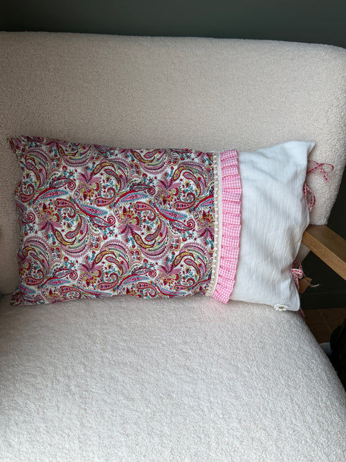 Coussin rectangulaire fait main, tissu imprimé cachemire rose et lin blanc, volant à carreaux vichy rose et rubans, posé sur fauteuil en bouclette blanche