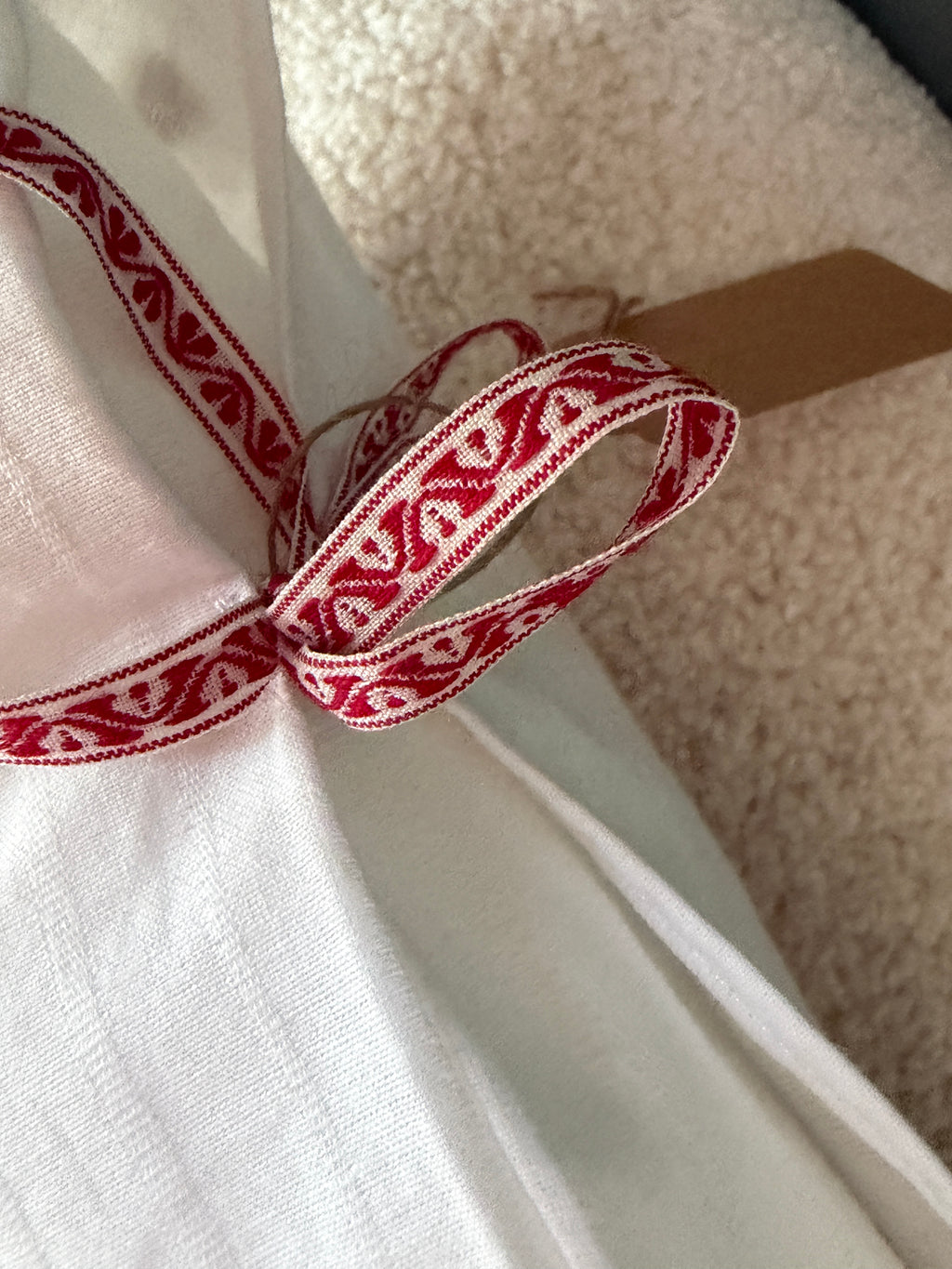 Détail coussin fait main, ruban brodé motif folklorique rouge et blanc noué sur lin blanc avec étiquette artisanale