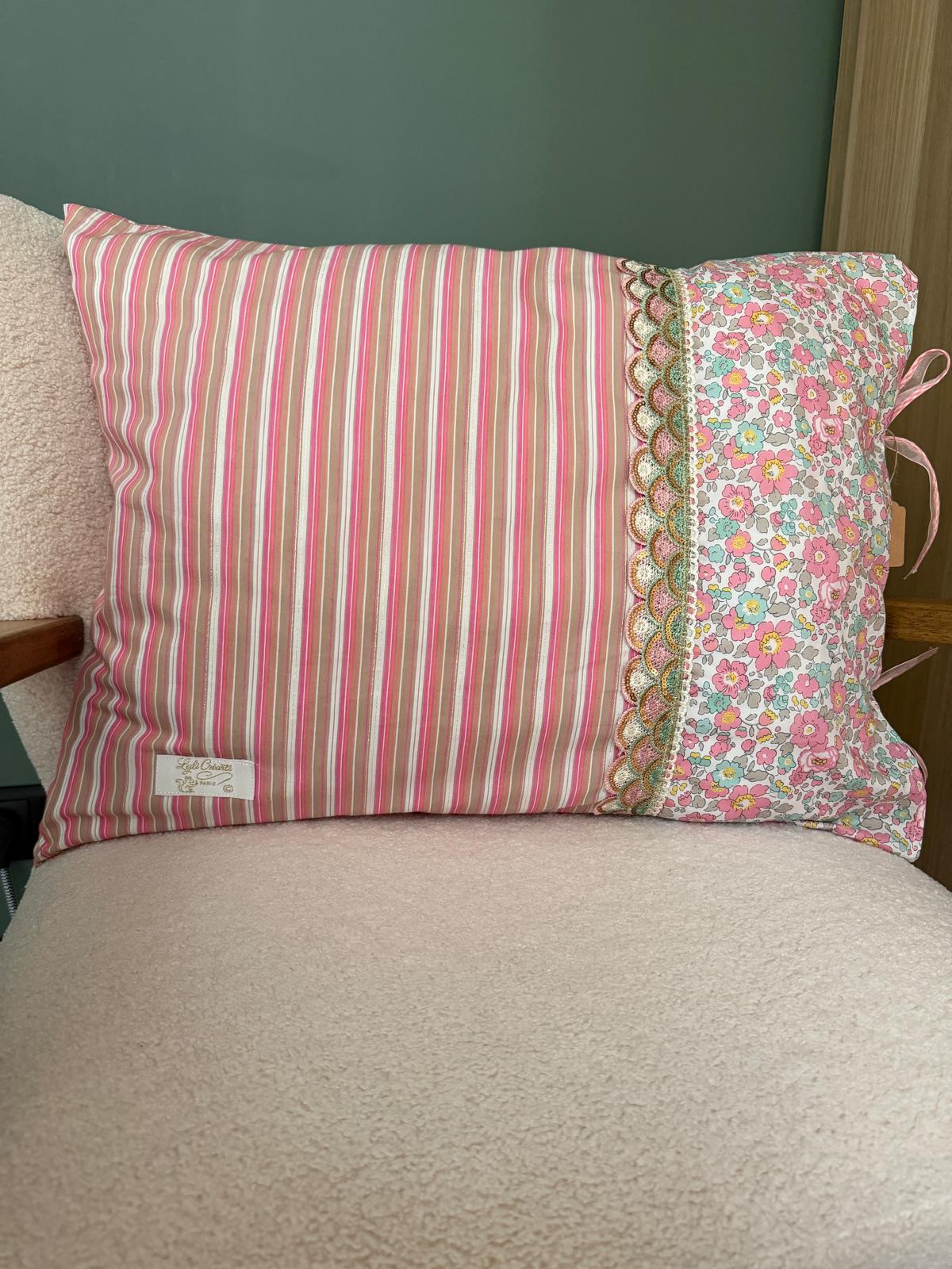 Coussin rectangulaire fait main Lyli Créarti, tissu rayé rose et taupe et imprimé fleuri liberty, galon écaille brodé, posé sur fauteuil en bouclette blanche