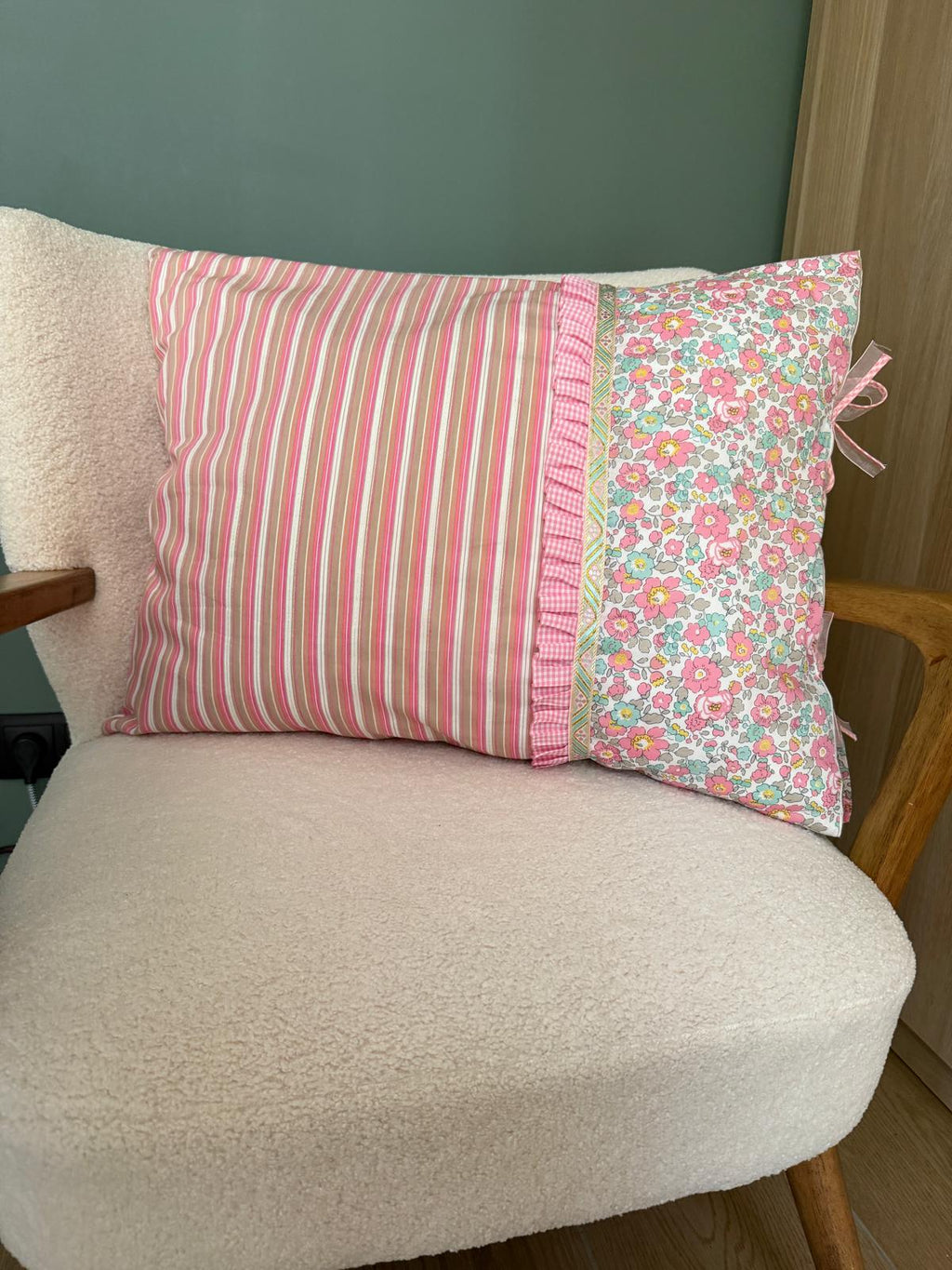 Coussin carré fait main Lyli Créarti, tissu rayé rose et taupe et imprimé fleuri liberty, volant vichy rose, posé sur fauteuil en bouclette blanche