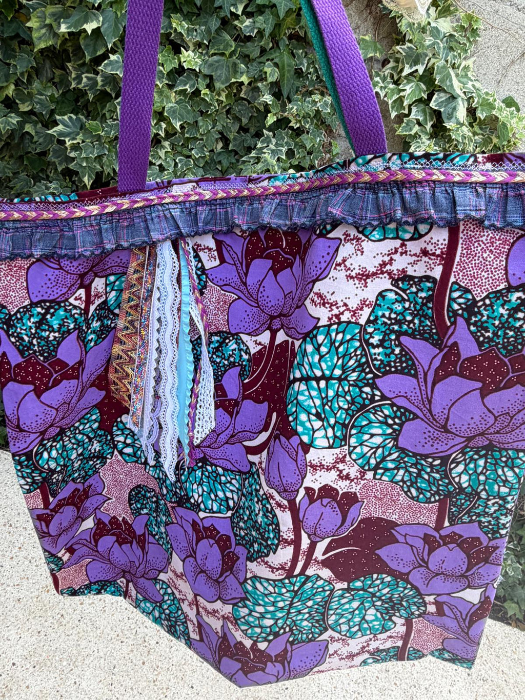 Sac cabas fait main Lyli Créarti en extérieur, tissu wax imprimé fleurs de lotus violet et turquoise, volant écossais et anses tressées violettes