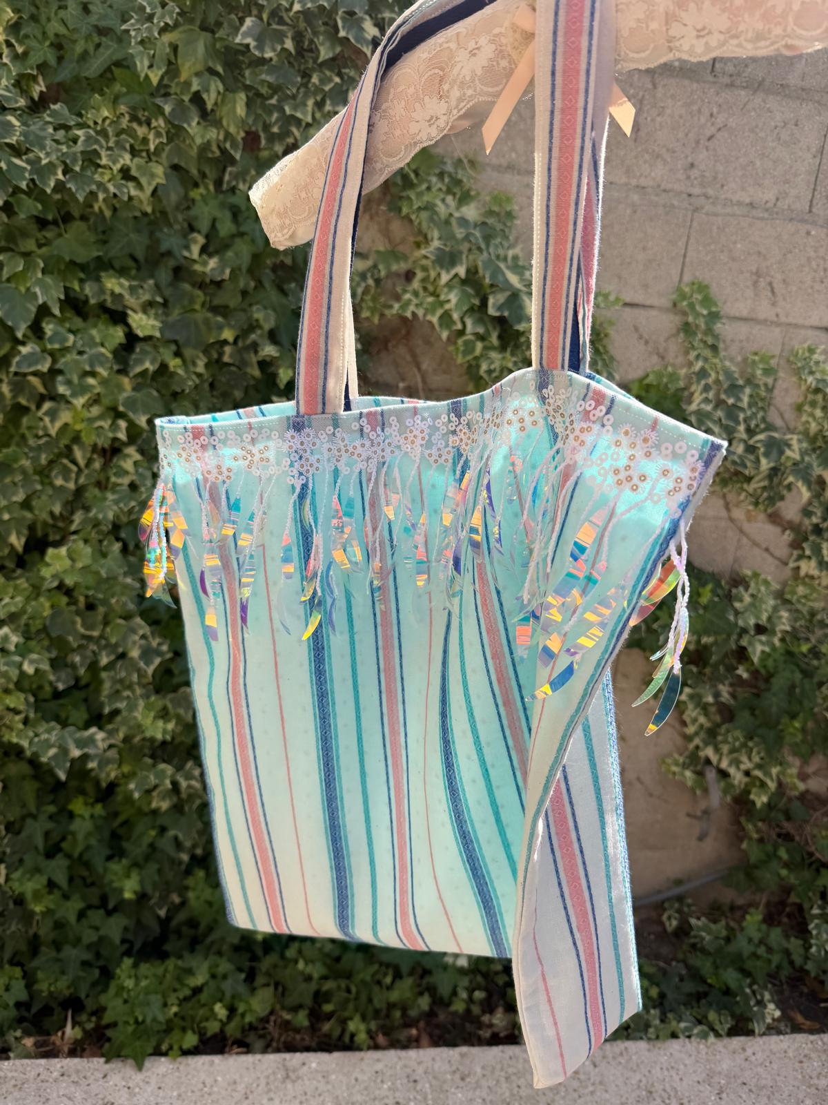 Sac cabas fait main Lyli Créarti suspendu en extérieur, tissu rayé pastel avec franges holographiques et bordure fleurie brodée
