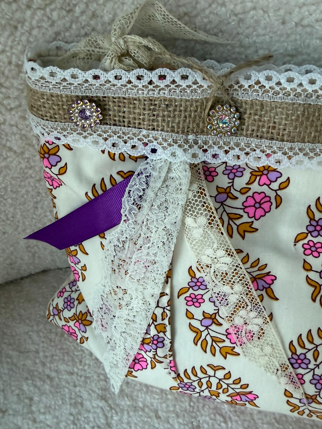 Zoom bourse fait main Lyli Créarti, tissu imprimé fleuri rose et doré, bordure toile de jute et dentelle avec strass, ruban violet et voile en dentelle