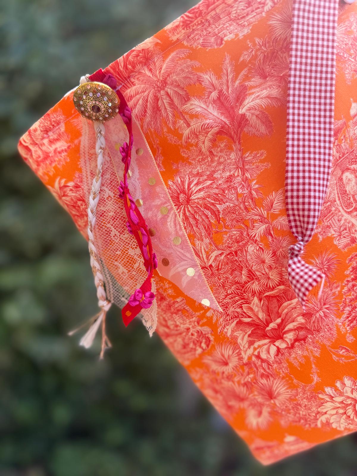 Zoom bourse fait main en extérieur, tissu toile de Jouy orange motif palmiers avec bouton bijou, tulle doré et anse à carreaux vichy rouge