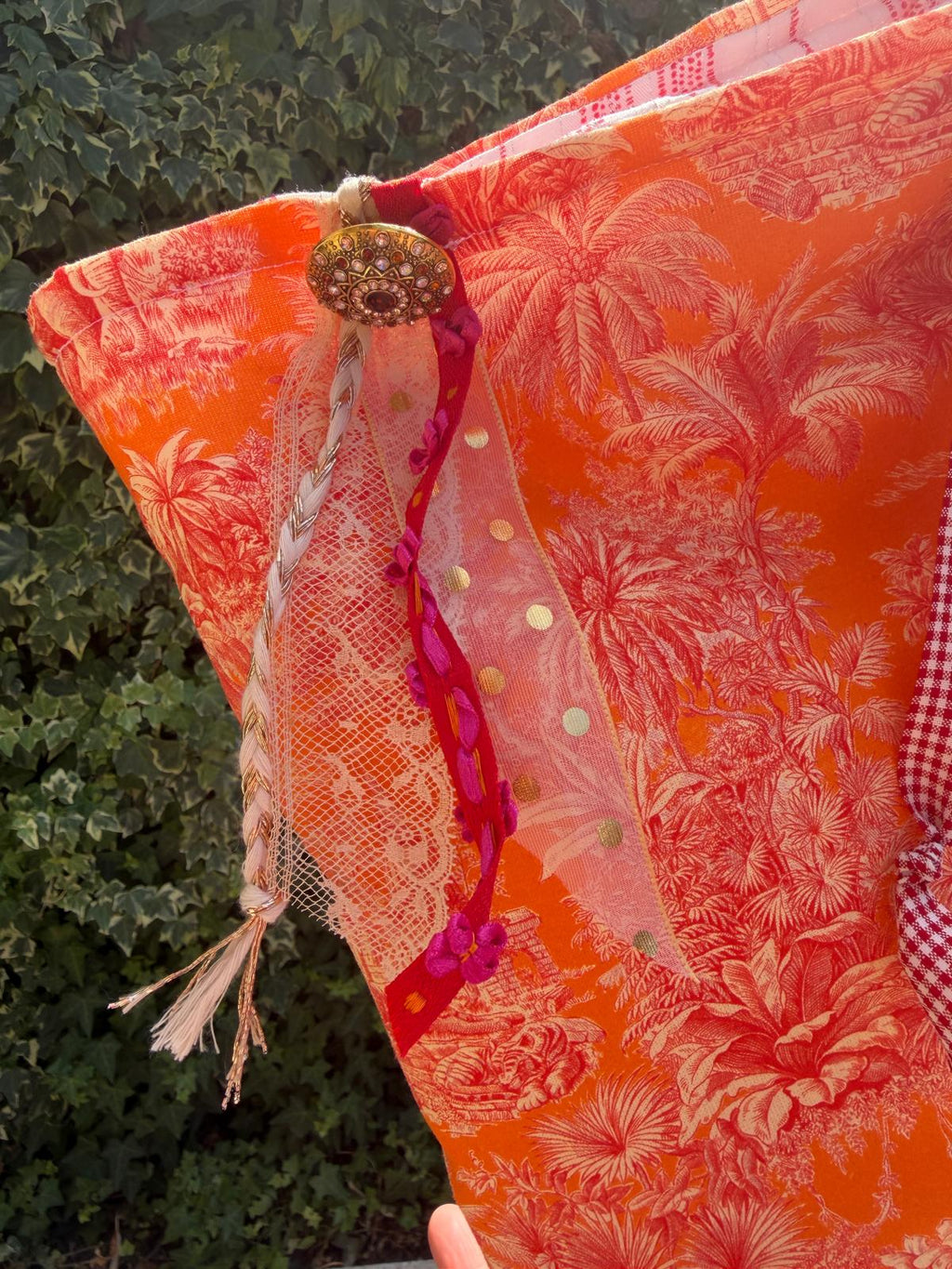 Zoom bourse fait main, ouverture en tissu toile de Jouy orange motif palmiers avec bouton bijou, tulle doré et rubans fuchsia