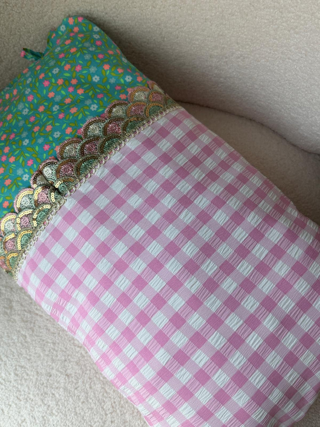 Coussin fait main vue de dessus, tissu vichy rose et imprimé fleuri turquoise avec galon écaille brodé, posé sur plaid en bouclette blanche