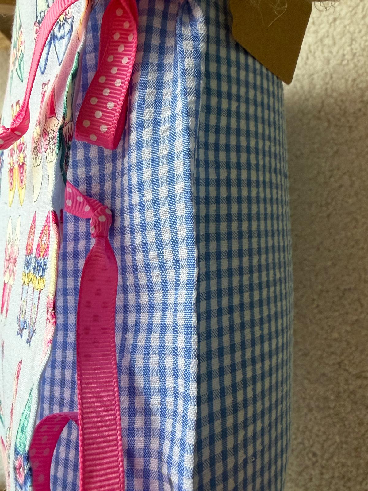 Détail coussin fait main, angle en tissu vichy bleu et blanc avec ruban à pois rose et bord imprimé motifs fleuris