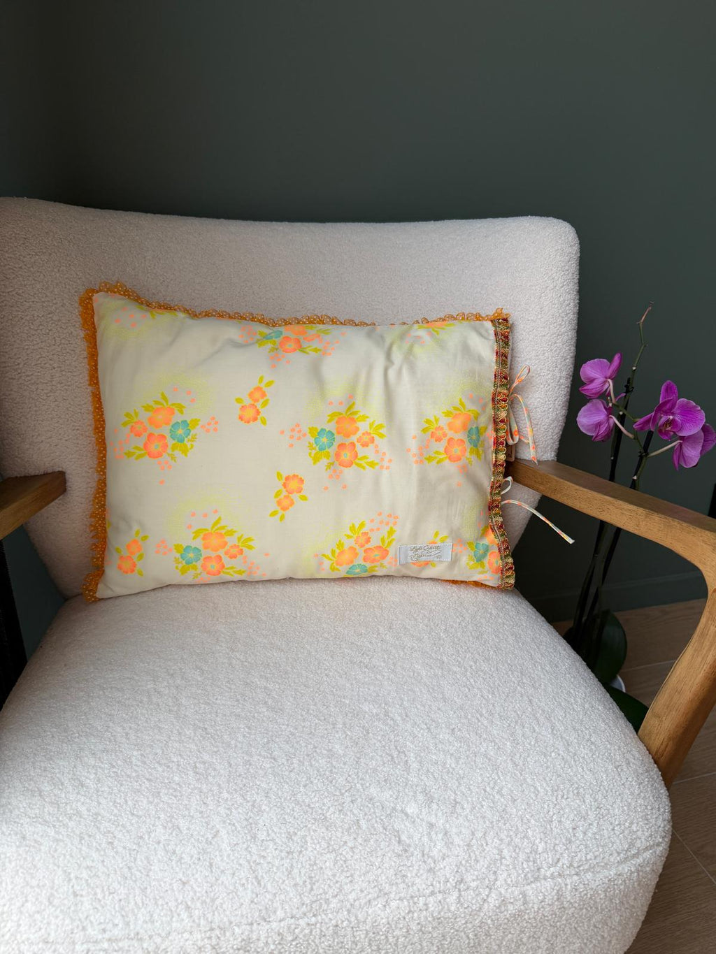 Coussin en coton vintage fleuri orange et jaune posé sur un fauteuil en bouclette écrue, cousu main