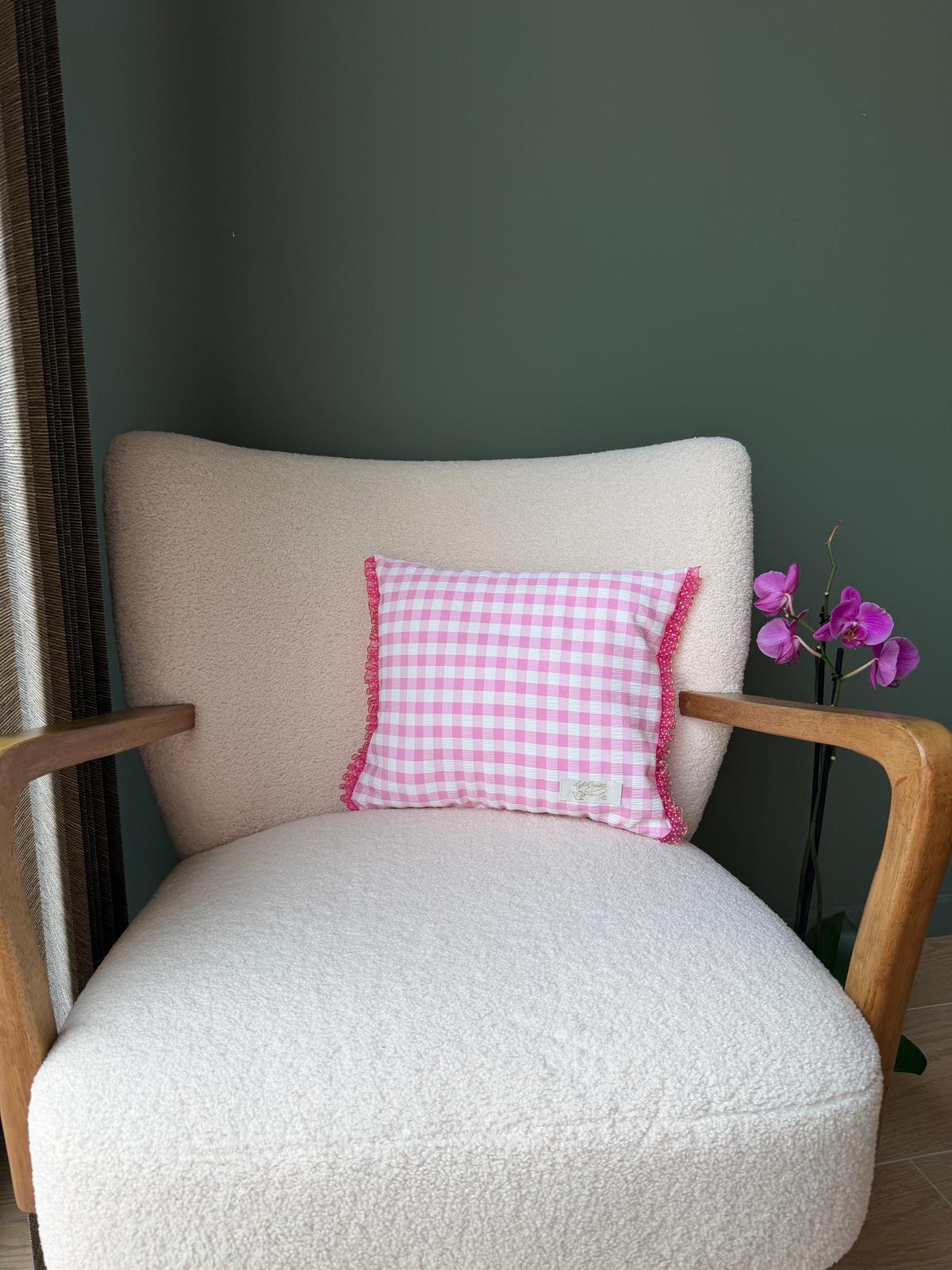 Verso du coussin en vichy rose et blanc, galon rose festonné, posé sur un fauteuil en bouclette écrue